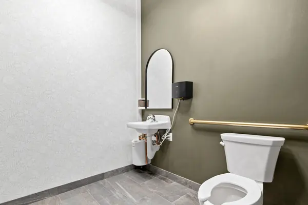 Private restroom with sage walls, arched mirror and brass fixtures