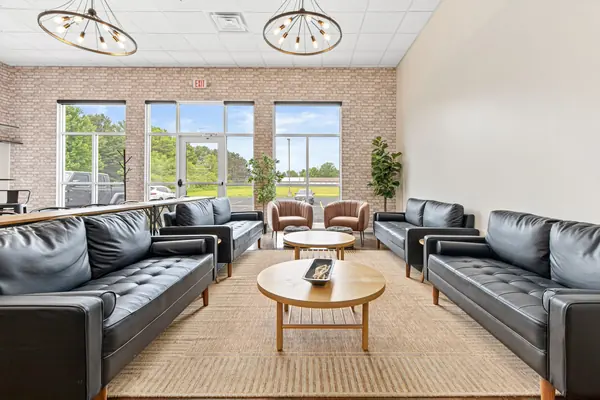 Symmetrical lounge: two pairs of black leather sofas around oak coffee tables, brick wall and tall windows